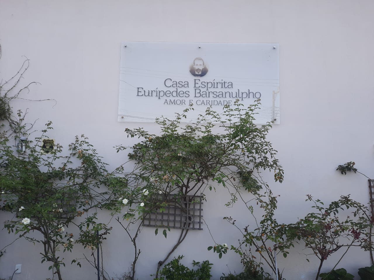 A placa da Casa Espírita Eurípedes Barsanulpho na fachada, entre roseiras